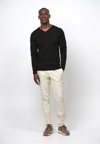 Svart V-ringad tröja, krämfärgade chinos och bruna sneakers. Slätt tyg med en figurnära design, minimala detaljer och en neutral färgpalett.