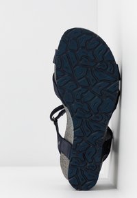 Navy blue sandal with a textured rubber sole and a cork footbed. Features adjustable straps and a flat design for casual wear.