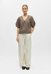 Haut marron à manches courtes avec un col en V et un détail de boutons, assorti à un pantalon large de couleur crème et des chaussures noires sans lacets.