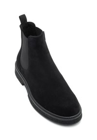 Mustad musta suede jalats, millel on elastsed külgpaneelid, tekstureeritud kummitald ja kätetõstmine lihtsaks selga tõmbamiseks. Suur ja minimalistlik disain.