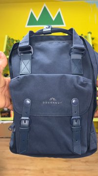 Navy blue canvas backpack with leather accents, front pocket flap, adjustable straps, and a logo displaying mountains. Sturdy construction details.