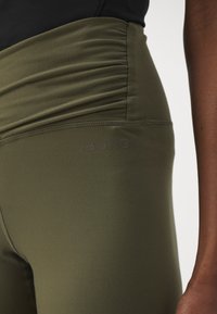 Ελαιόχρουν κολάν φτιαγμένα από λεία, ελαστική ύφανση, με συγκεντρωμένο σχέδιο στη μέση και διακριτό λογότυπο "BORG" στο πλάι.