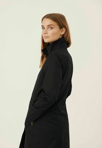 Black long coat with a high collar, featuring a sleek design, smooth texture, and minimalistic style. Side pockets and a modern silhouette.