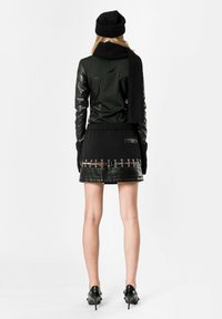 Chaqueta de cuero negra con mangas largas, combinada con una bufanda y un sombrero de punto negro. La falda negra ajustada presenta acentos horizontales y herrajes.