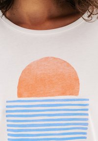 T-shirt bianca con una grafica di un sole arancione sopra strisce orizzontali blu, con una texture morbida e un collo rotondo casual.