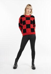 Rood en zwart geblokt gebreid sweater met een relaxte pasvorm, geribbelde halslijn en lange mouwen, gecombineerd met zwarte aansluitende broek en chunky laarzen.