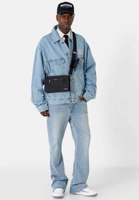 Chaqueta de denim azul claro sobre una camiseta blanca, combinada con jeans azul claro y zapatillas blancas. Un bolso cruzado negro descansa sobre la chaqueta.