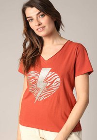 Rustkleurige V-hals t-shirt van katoen, met een zilveren glitterhart met een zebra patroon en een bliksemflitsontwerp op de voorkant.