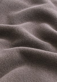 Tissu tricoté texturé de couleur brune atténuée, présentant une surface douce et ondulée avec des motifs de tissage complexes et une finition lisse.