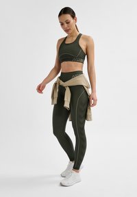 Olivgrön träningsoutfit med en figursydd crop top och högmidjade leggings med zigzagmönster. Ljusbeige sweatshirt knuten i midjan.