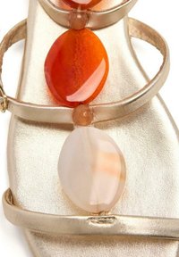 Sanda secundaria metálica dorada que presenta tres piedras ovaladas: una blanca translucida, una naranja y una melocotón. Las tiras son delgadas y elegantes en diseño.