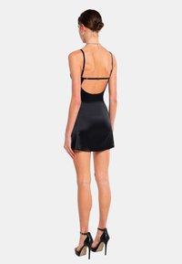 Zwart satijnen mini-jurk met een lage rug en dunne bandjes. Heeft een uitlopende rok en minimale hardwareaccenten. Gemaakt in combinatie met zwarte hoge hakken.