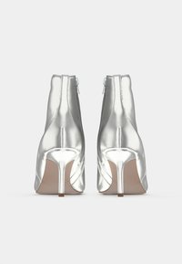 Hõbedased kõrged kontsaga pahkluu saapad, nähtavad tagantpoolt, külgsiiprite ja teravate kontsadega, valge taustal.