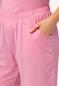 Pantaloni corti in cotone rosa con cintura elastica, dotati di tasche laterali e una texture morbida. Il design è ampio e informale.