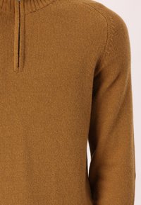 Pullover in maglia marrone con colletto alto, dotato di chiusura a zip quarti, dettagli a costine e una texture morbida. Vestibilità classica.