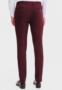Burgundowe spersonalizowane spodnie o gładkiej fakturze, z kieszeniami tylne i eleganckimi liniami prasowania. W połączeniu z czarnymi butami wizytowymi.