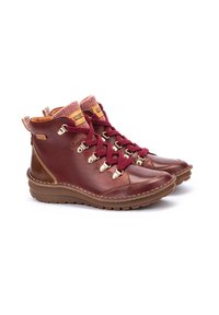 Bottes en cuir marron avec des lacets bordeaux, des accessoires dorés et un col en tricot texturé. Semelle en caoutchouc avec un motif de crampons.