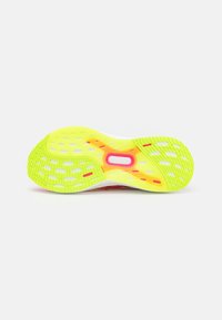 Semelle en caoutchouc jaune vif et rose d'une chaussure de course avec des grips texturés et un design perforé pour la traction et la flexibilité.