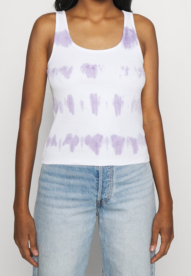 Camiseta sin mangas blanca con un patrón de tintado en púrpura, con escote redondeado y textura acanalada. Combinada con unos jeans de denim azul claro.