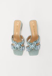 Een paar teal lederen schuifsandalen met een versierde bloemdesign met blauwe en heldere edelstenen, open teen en een blokhak.