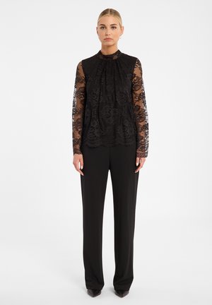 Zwarte kanten blouse met lange mouwen en een hoge hals, voorzien van bloemenpatronen en plooien, gecombineerd met zwarte wijde broek.