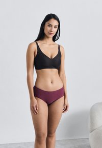 Črni nedrček brezšiven z izrezom v obliki črke V, združen z bordo visokim spodnjim perilom, oba iz gladkega, raztegljivega materiala.