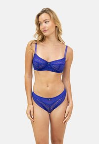 Ensemble de lingerie en dentelle de bleu profond, comprenant un soutien-gorge avec des bretelles réglables, un armature, et un nœud décoratif, associé à une culotte haute assortie.