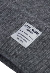 Šedá texturovaná tkanina s tkaným vzorem, která má obdélníkovou bílou etiketu s černým textem uvádějícím "PEPE JEANS LONDON."