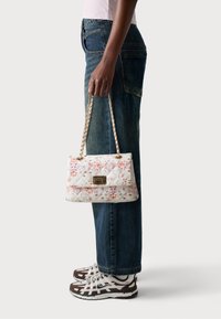 Vadderad vit handväska med blommigt mönster, guldhardware och kedja. Kombinerad med blå jeans och bruna och vita sneakers.
