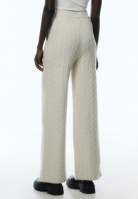 Witte gebreide wijde broek met kabelpatroon, hoge tailleband en gestructureerde stof. Sleek zwarte platformlaarzen complementeren de outfit.