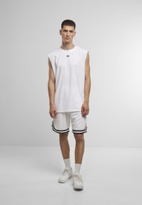 Hvid ærmeløs bomulds T-shirt med et lille logo, parret med hvide shorts med sorte sidelister, båret med hvide sneakers.