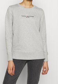 Grå sweatshirt i bomullsblandning med rund hals, ribbade ärmslut och fåll, med broderad "TOMMY HILFIGER EST. 1985"-logga på bröstet.