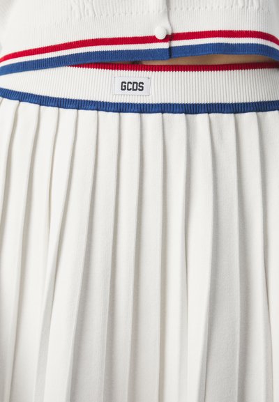 Jupe plissée blanche avec une ceinture à rayures rouges et bleues, arborant une étiquette "GCDS". Le matériau semble doux et texturé.