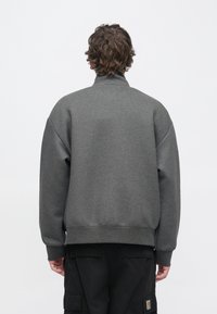 Grauer Pullover mit hohem Kragen und überschnittenen Schultern, mit glatter Textur und geripptem Saum, kombiniert mit schwarzen Cargo-Hosen.