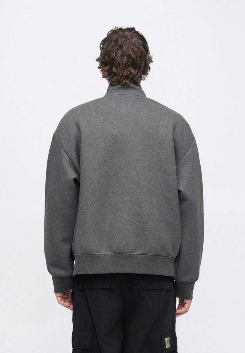 Sweat-shirt gris avec un col montant et des épaules tombantes, présentant une texture lisse et un ourlet côtelé, porté avec un pantalon cargo noir.