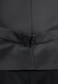 Musta kangasklipsi, jossa on kaksoisnauhamallin suljenta. Materiaali on sileä, jossa on hieno kiilto, ja se on täydentänyt siisteillä, jyrkillä linjoilla.