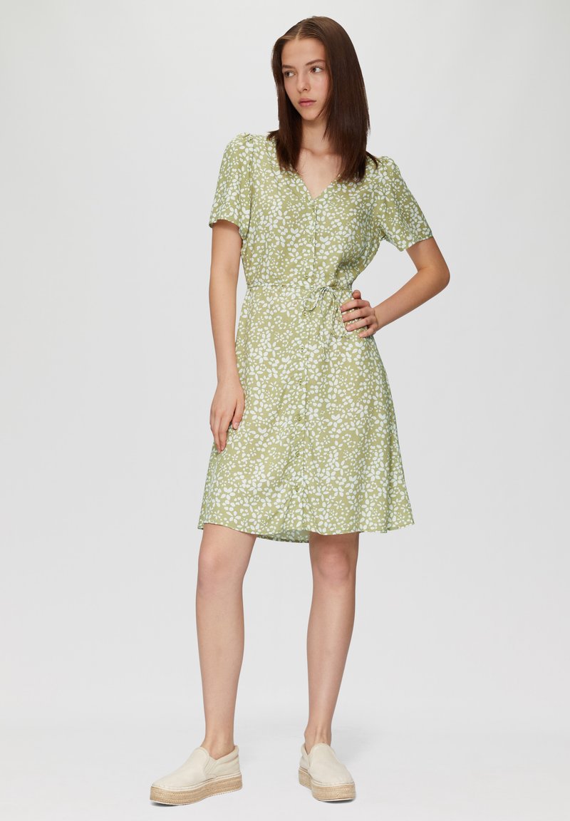 Zielona kwiecista sukienka z dekoltem w serek, krótkimi rękawami, talią ze sznurkiem i zwiewną spódnicą; w połączeniu z beżowymi espadrylami.