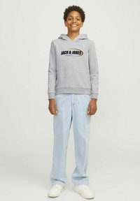 Felpa grigia con logo frontale, coulisse, polsini e orlo a costina, abbinata a jeans dritti azzurri e sneakers bianche.