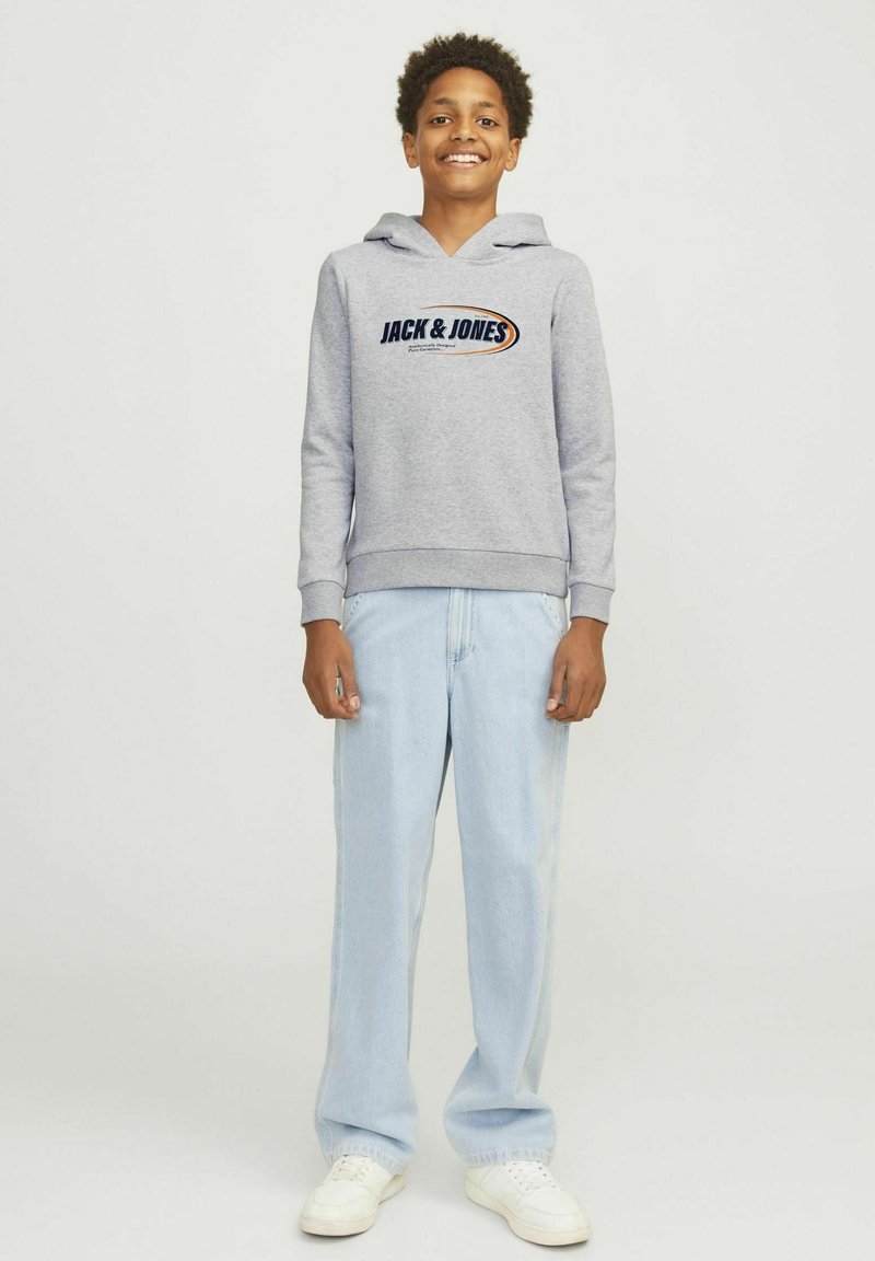 Felpa grigia con logo frontale, coulisse, polsini e orlo a costina, abbinata a jeans dritti azzurri e sneakers bianche.