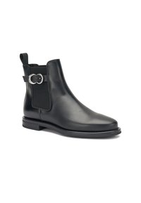 Botas de tobillo de cuero negro con paneles elásticos, acento de herrajes plateados circulares, puntera redondeada y tacón bajo apilado. Textura suave.