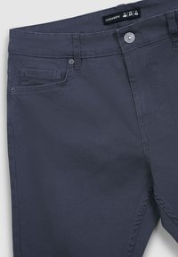 Granatowe bawełniane spodnie o prostym kroju, z kieszeniami z przodu i metalowym zapięciem. Metka wskazuje rozmiary: ITA 46, USA 31, EU 42.