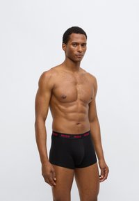 Black boxer briefs with a red "HUGO" logo on the waistband, made from smooth fabric, fitting close to the body. No additional patterns present.