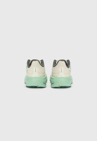 Zapatillas de correr con una parte superior de un color beige claro, acentos en gris oscuro y suela verde menta. Material texturizado con un diseño en capas y un acolchado prominente.