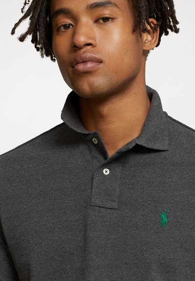 Tumed hall polo-särk, mis on valmistatud tekstureeritud kangast, klassikalise krae, kolme nupuga nööbirea ja rinnal rohelise brodeeritud logoga.