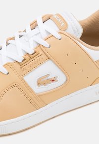 Lacoste sneakers med en överdel i beige och vit läder. Funktioner inkluderar vita snörningar, en texturerad beige tunga och en logopatch med ett krokodilmotif.