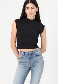 Top court sans manches noir avec col montant en tissu lisse, associé à un jean taille haute bleu clair avec un design classique à cinq poches.