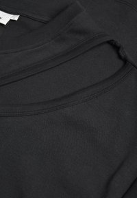 T-shirt en coton noir avec col rond et tissu texturé. Le design comprend des couches superposées au niveau du col.