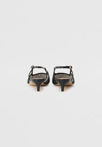 Paire de sandales à talons petits noirs en cuir avec brides autour de la cheville et boucles dorées, vues de dos sur un fond blanc.