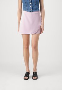 Rosa sateng mini skjørt med en subtil asymmetrisk kant, parret med en denim crop topp med knapper og en tettsittende design. Svart åpen tå mule.