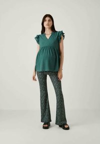 Τυρκουάζ μπλούζα με φουσκωτά μανίκια και V-λαιμόκοψη, συνδυασμένη με φαρδιά παντελόνια που έχουν ένα μικρό floral σχέδιο σε λευκό και πράσινο. Λείο υλικό.